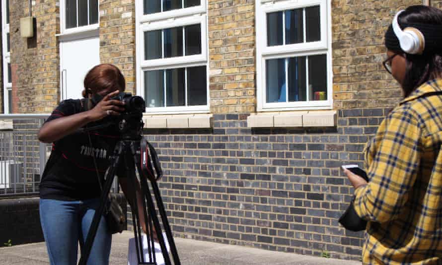 Two young women, one behind a camera, the other presenting to camera; both part of a summer school run by Ghetto Film School last year.