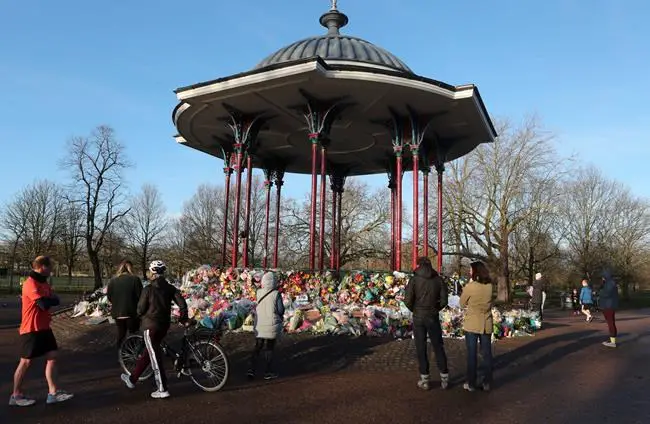 People pay their respects and look at the floral tributes placed at the bandstand in Clapham Common on Sunday, March 14, 2021, in memory of Sarah Everard who was abducted and murdered after last being seen walking home from a friend's apartment in south London on the night of March 3. Hundreds of people in London defied coronavirus restrictions Saturday to pay their respects to Everard who disappeared while walking home and was found dead a week later. (AP Photo/Tony Hicks)
